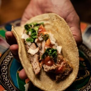 Close-up of a hand holding a delicious Mexican taco with fresh toppings.